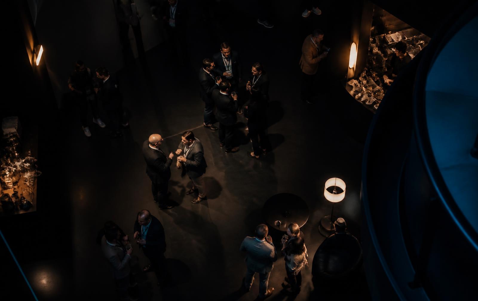 Overhead view of guests gathered in small groups in a dimly lit networking lounge
